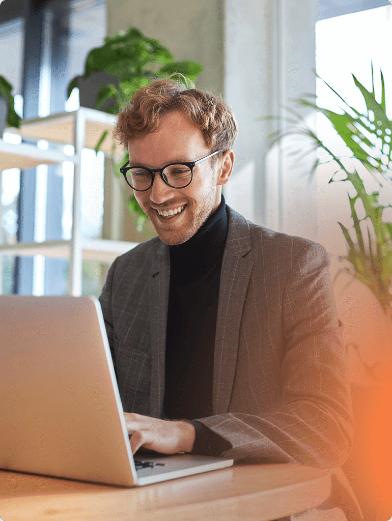 Homem sorrindo utilizando seu notebook sentado em uma mesa realizando uma analise de riscos psicossociais